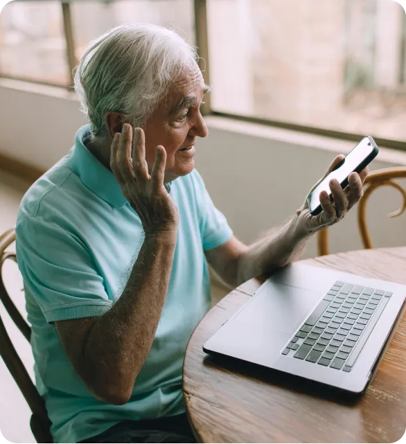 Elderly man using a laptop with assistance, symbolizing digital inclusion or telemedicine.